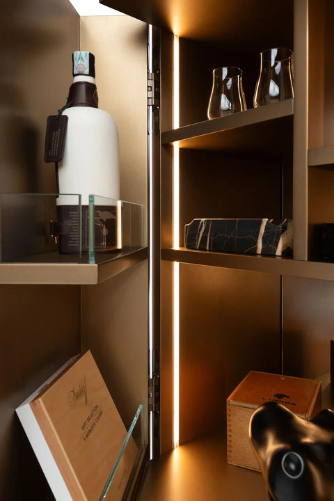 Interior of a bespoke bar cabinet with integrated LED lighting, a glass-edged shelf, a bottle and glasses